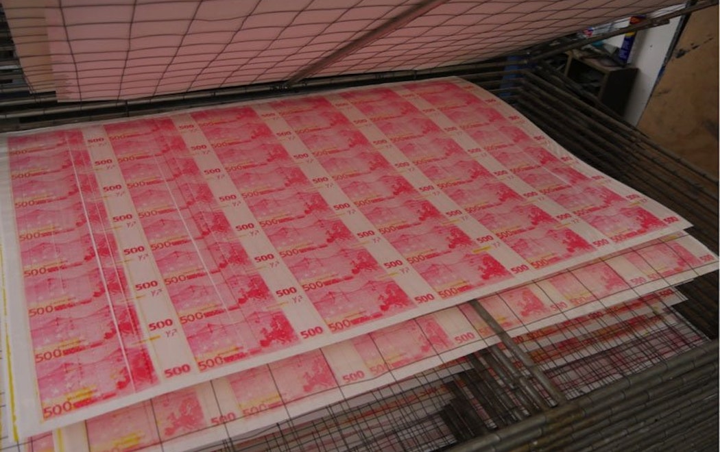 Large sheets of pinkish printed money dry on a multilayered drying rack